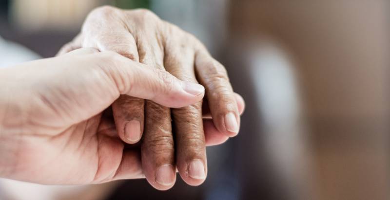 Pflegende Person hält die Hand eines älteren Menschen – Symbolbild