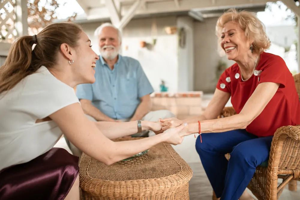 Junge Frau und älteres Paar lachen bei einem Gespräch auf einer Terrasse